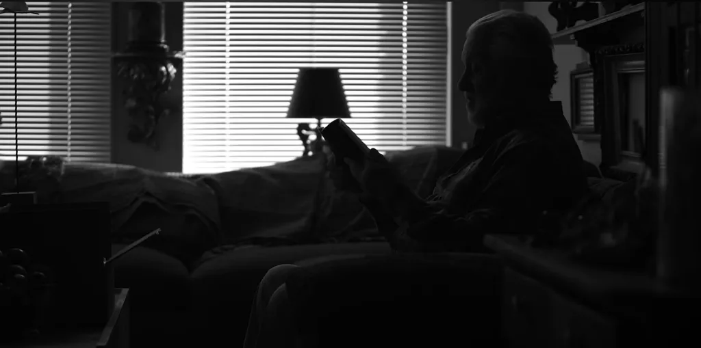 Black and white video capture of Steven Bridgens reading from his poetry collection. Bridgens is mostly seen in silhouette.