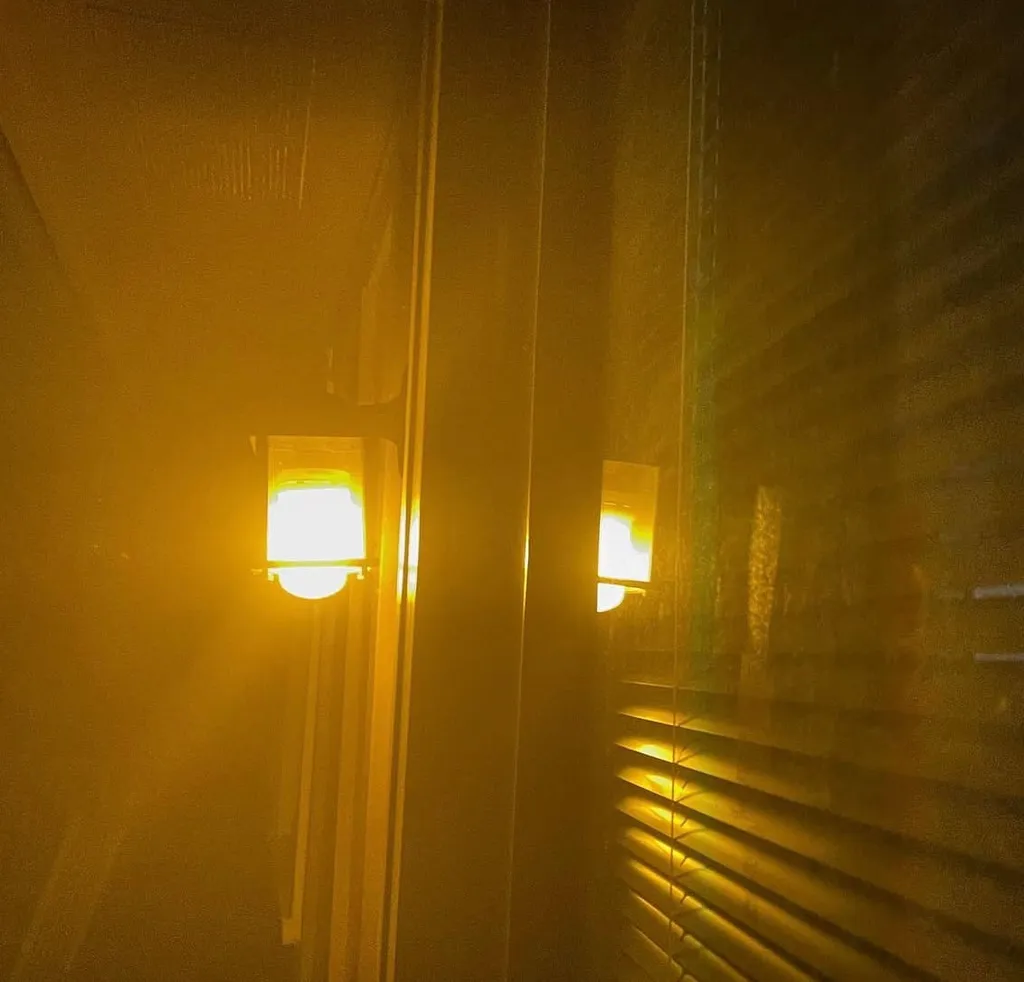 A porch light glows through a misty fog giving off a gold-amber glow.